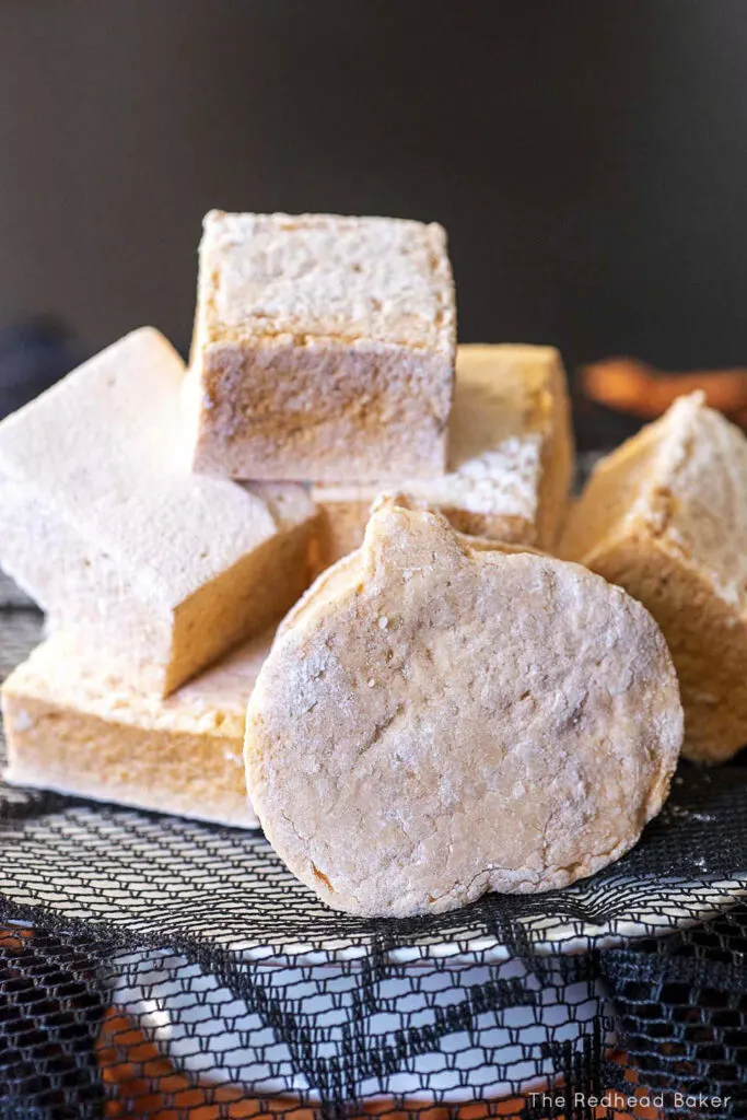 A pile of square and pumpkin-shaped marshmallows on a white cake stand