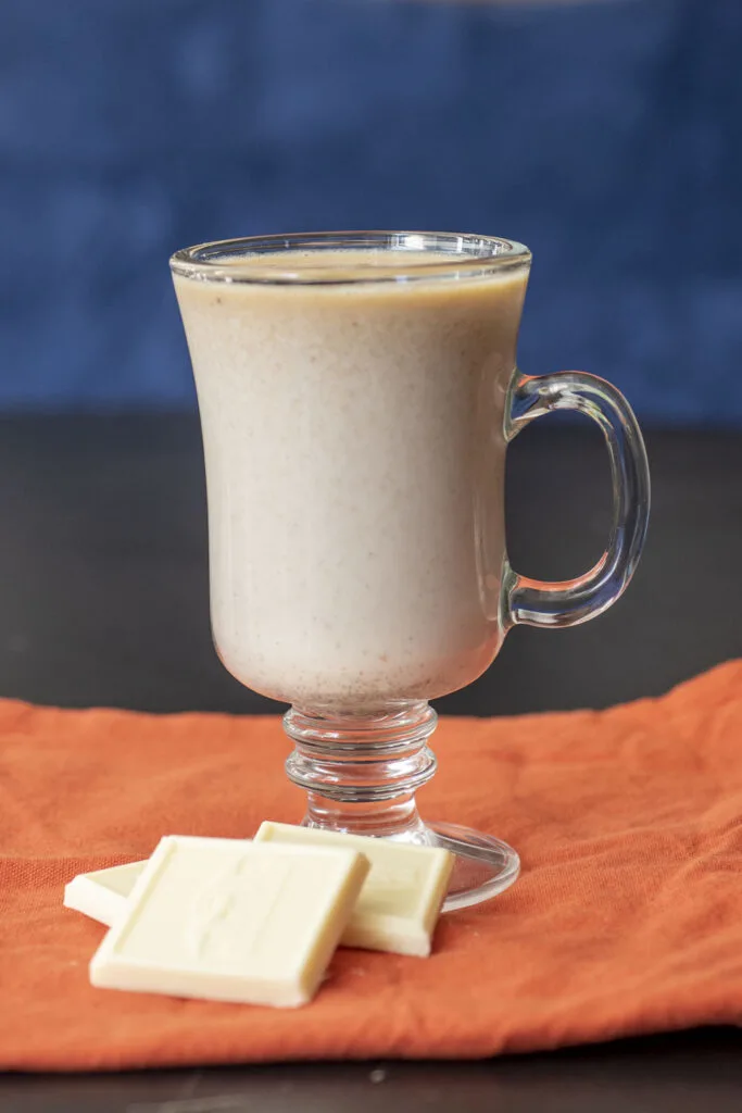 A mug of hot chocolate on an orange napkin in front of three squares of white chocolate baking bar