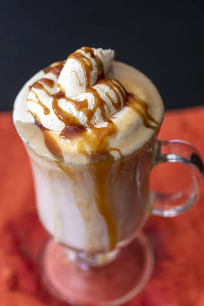 An overhead shot of a mug of white hot chocolate topped with caramel whipped cream and caramel drizzle