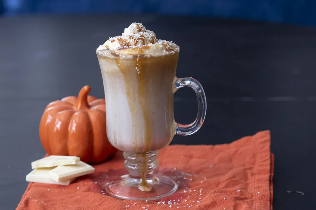 A mug of pumpkin white hot chocolate topped with caramel whipped cream and caramel drizzle