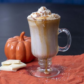 A mug of pumpkin white hot chocolate topped with caramel whipped cream and caramel drizzle