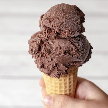 A child's hand holding a sugar cone with two scoops of chocolate ice cream