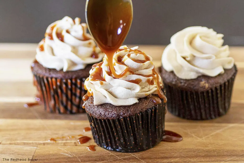Caramel being drizzled onto one of three frosted cupcakes