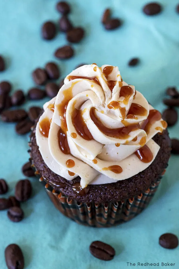 A pumpkin spice latte cupcake on a blue napkin, surrounded by coffee beans