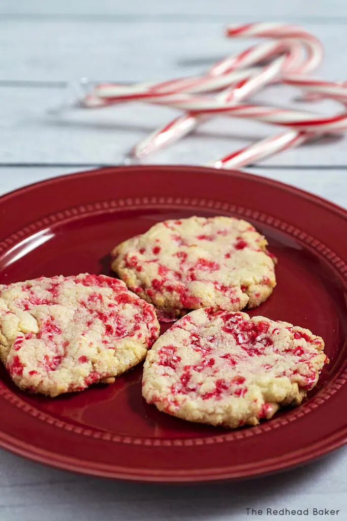 Three cookies on a red plate with some candy canes in the background