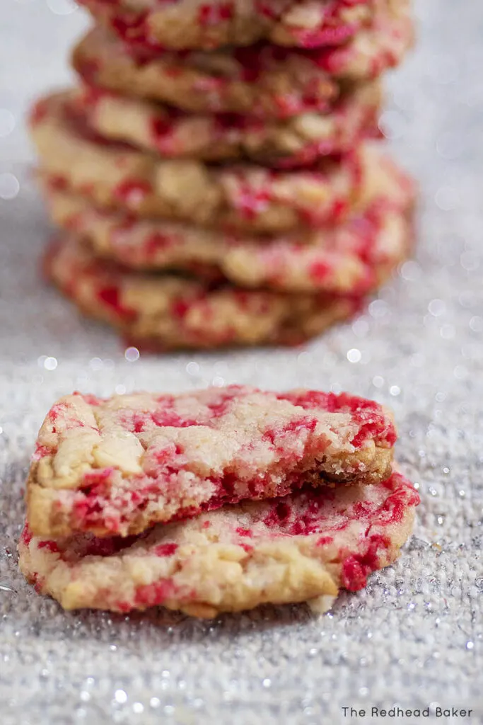 Two halves of a candy cane white chocolate cookie in front of a stack of cookies