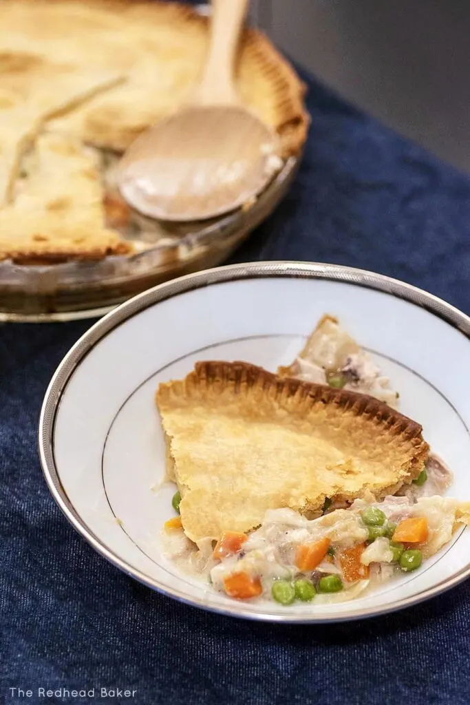 A wedge of chicken pot pie in a shallow bowl, with the pie plate in the background