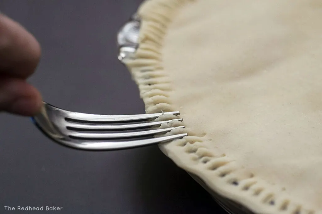 A fork crimping together the top and bottom pie crusts of a pot pie