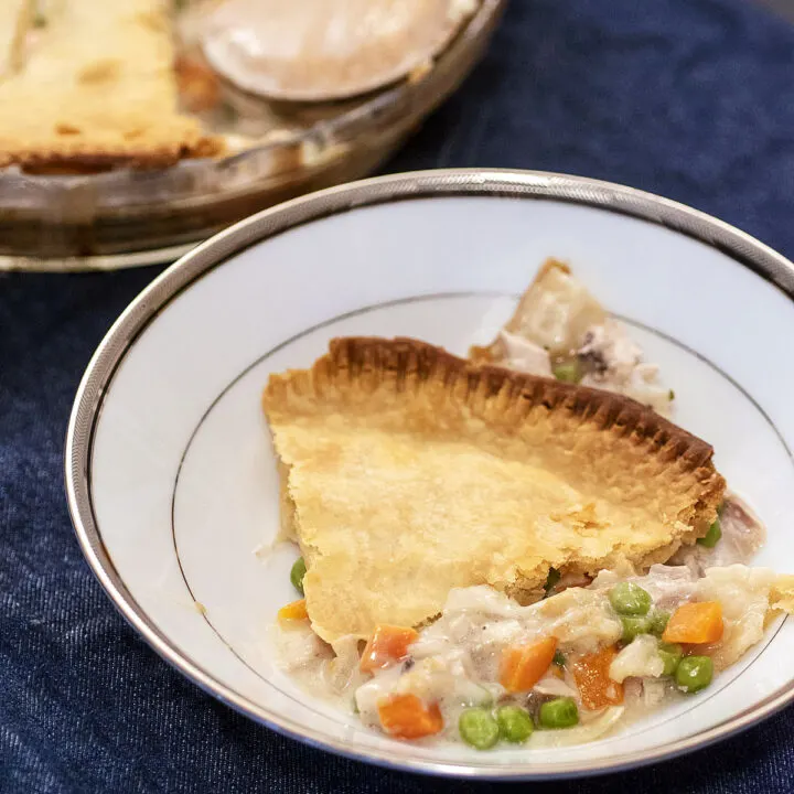 A shallow bowl with a wedge of chicken pot pie on a dark blue background