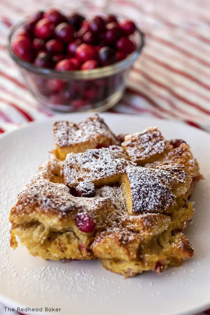 A close-up of a plate of French toast bake in front of a dish of fresh cranberries