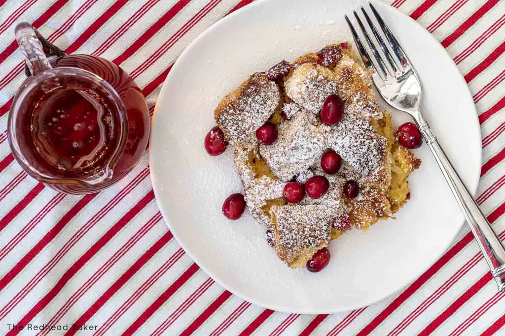 An overhead shot of cranberry eggnog French toast bake on a white plate, on a red and white striped napkin