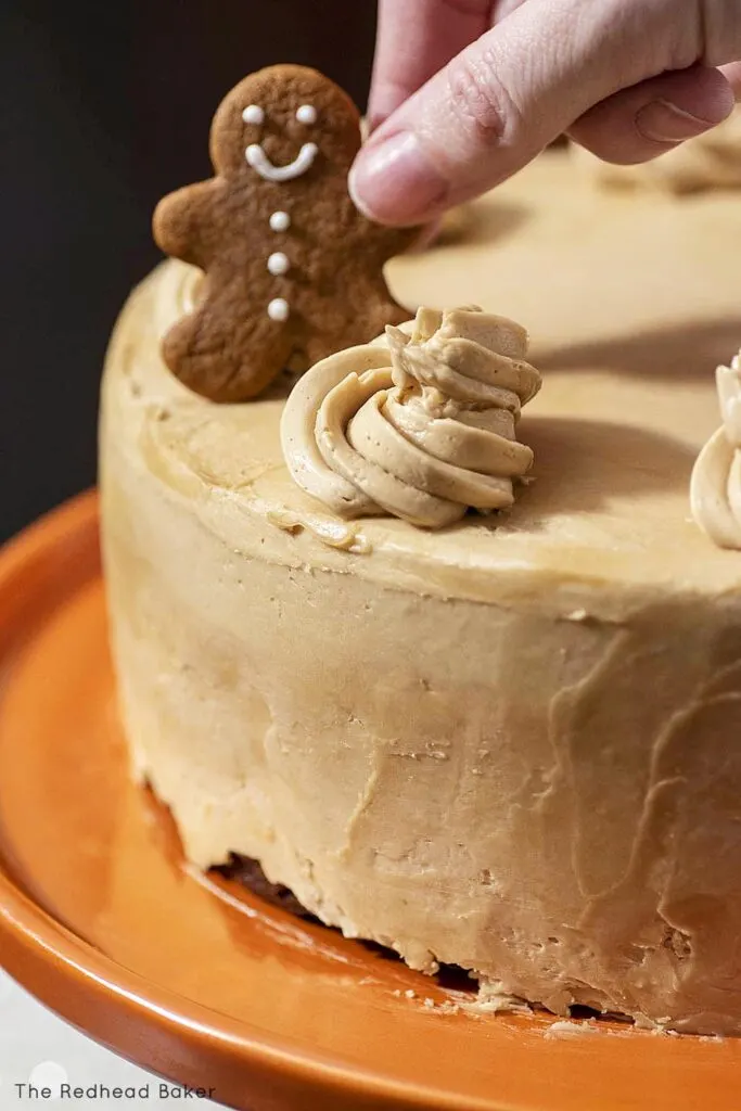 A hand placing a mini gingerbread man on top of a frosted cake