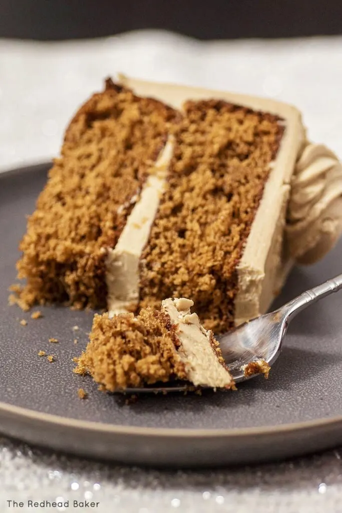 A slice of gingerbread layer cake on its side on a plate with a fork full of cake