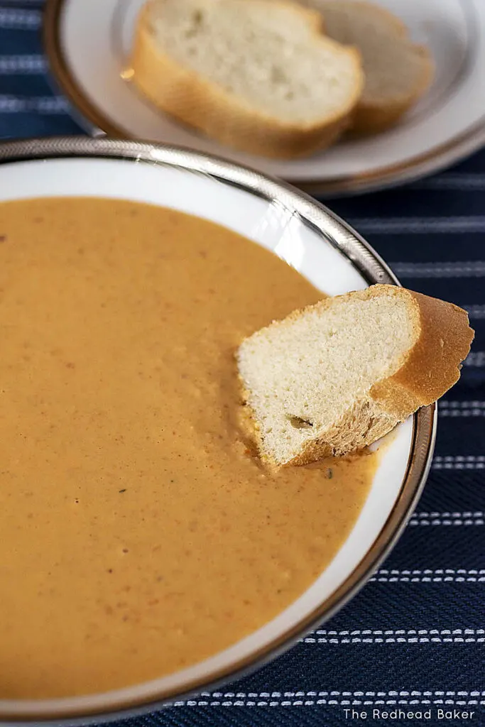 A slice of baguette half-dunked in a bowl of soup