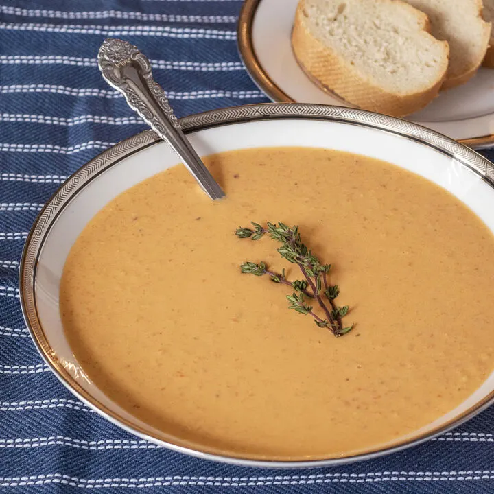 A soup bowl of lobster bisque in front of a plate of baguette slices