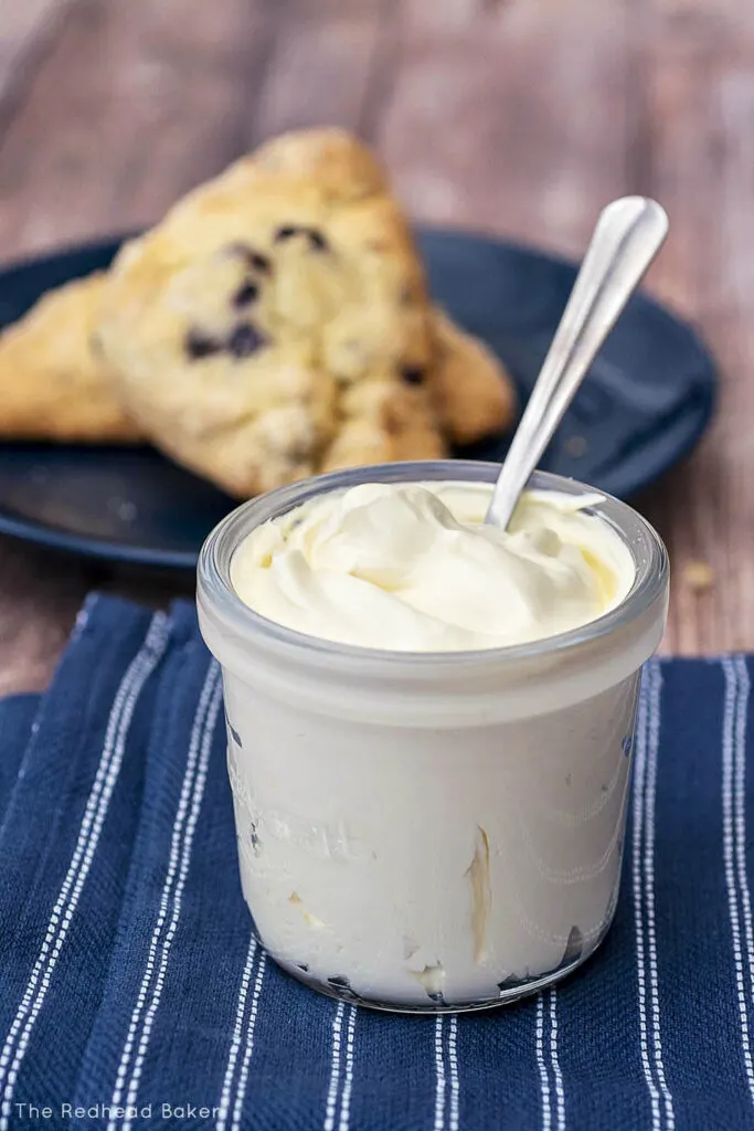 A full jar of clotted cream in front of a plate of blueberry scones