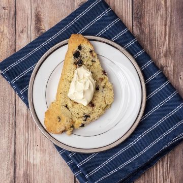 A blueberry scone topped with clotted cream on a white plate