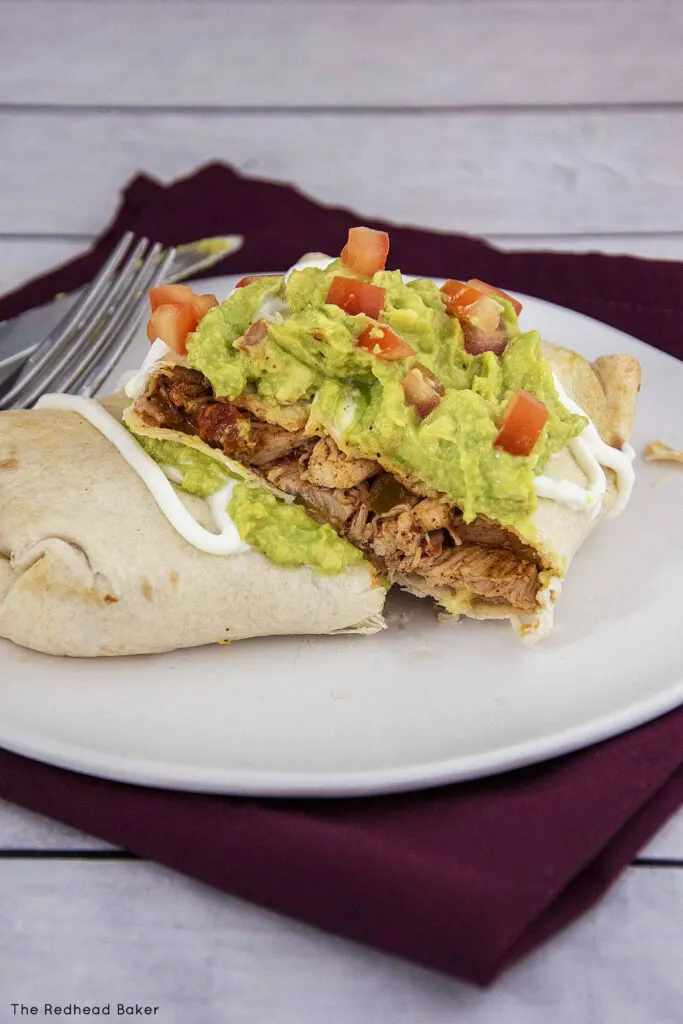 A cut-open chimichanga on a while plate with a knife and fork