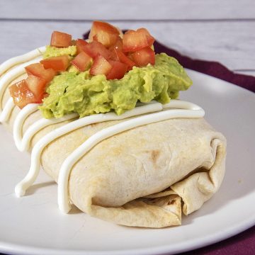 A chicken chimichanga on a white plate, topped with mashed guacamole and diced tomato