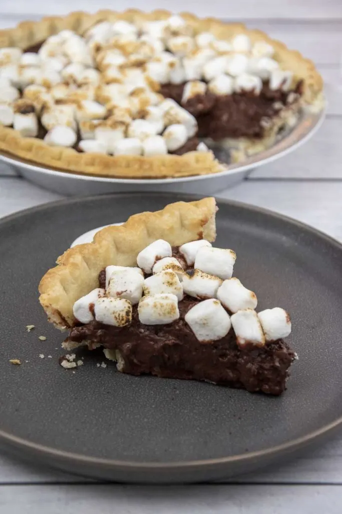 A slice of s'mores pie on a plate in front of the rest of the pie