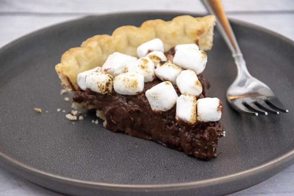 A close-up of a slice of s'mores pie on a gray plate with a fork