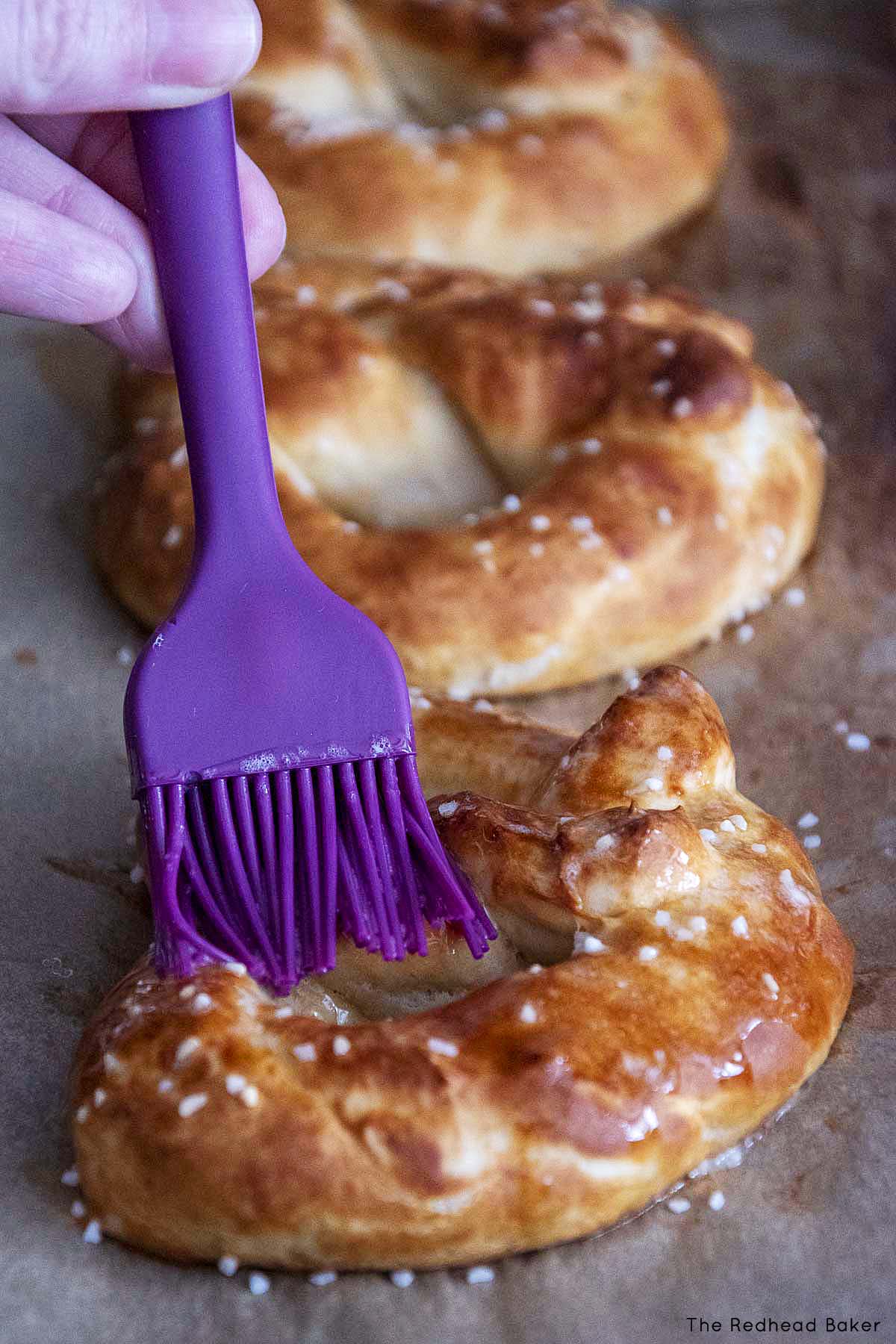 Baked soft pretzels being brushed with melted butter.