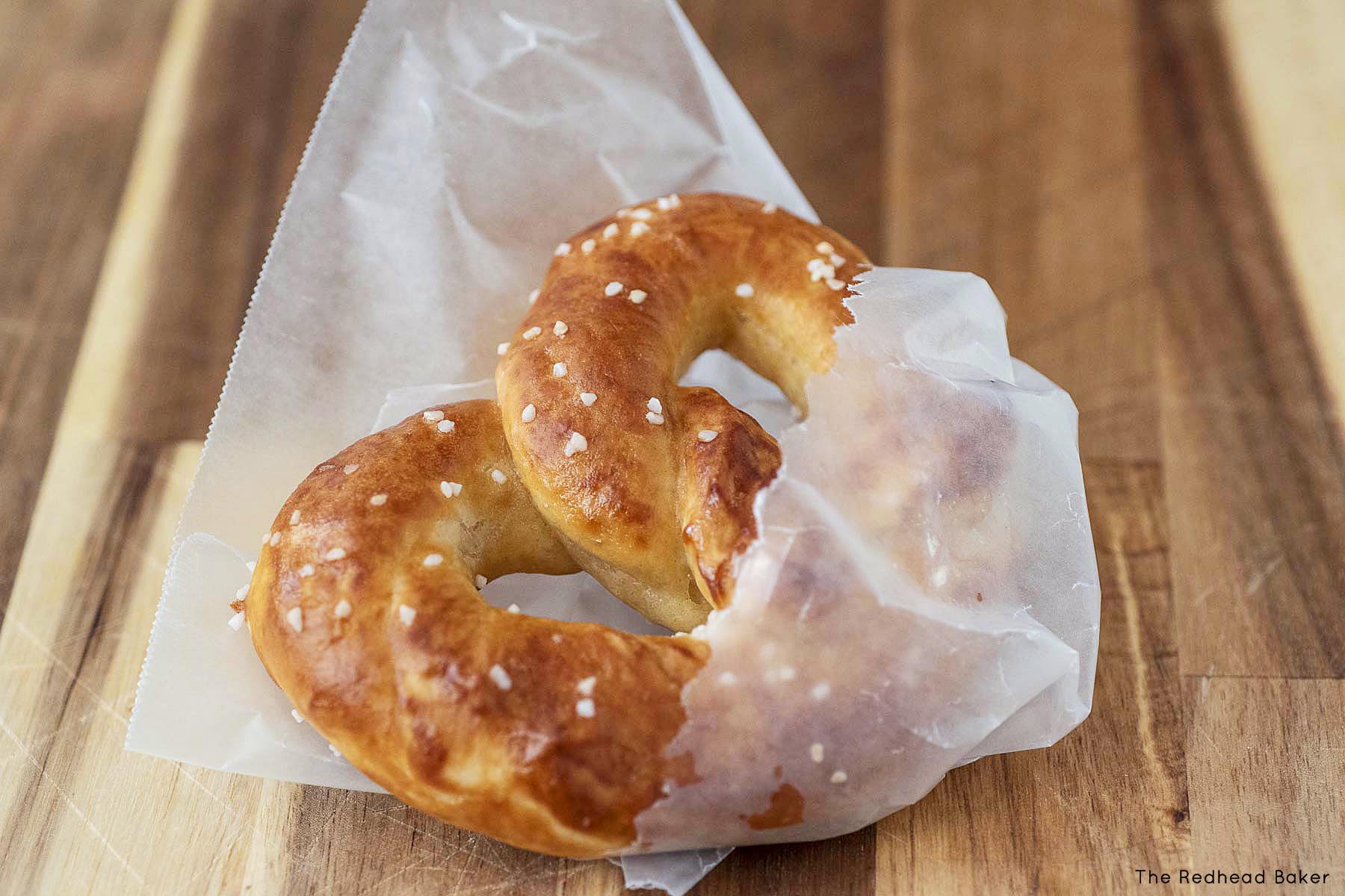 A soft pretzel wrapped in wax paper on a wooden board.