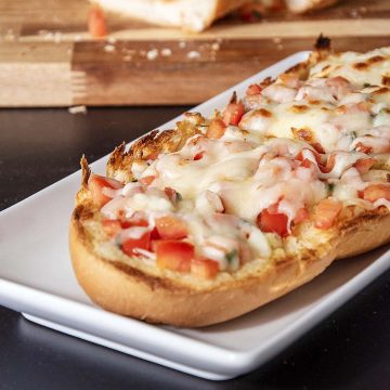 Sliced cheesy bruschetta garlic bread on a white serving tray