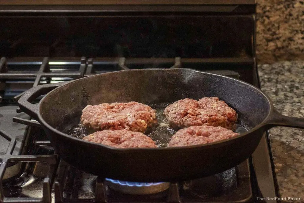 Four burger patties cooking in a cast-iron skillet