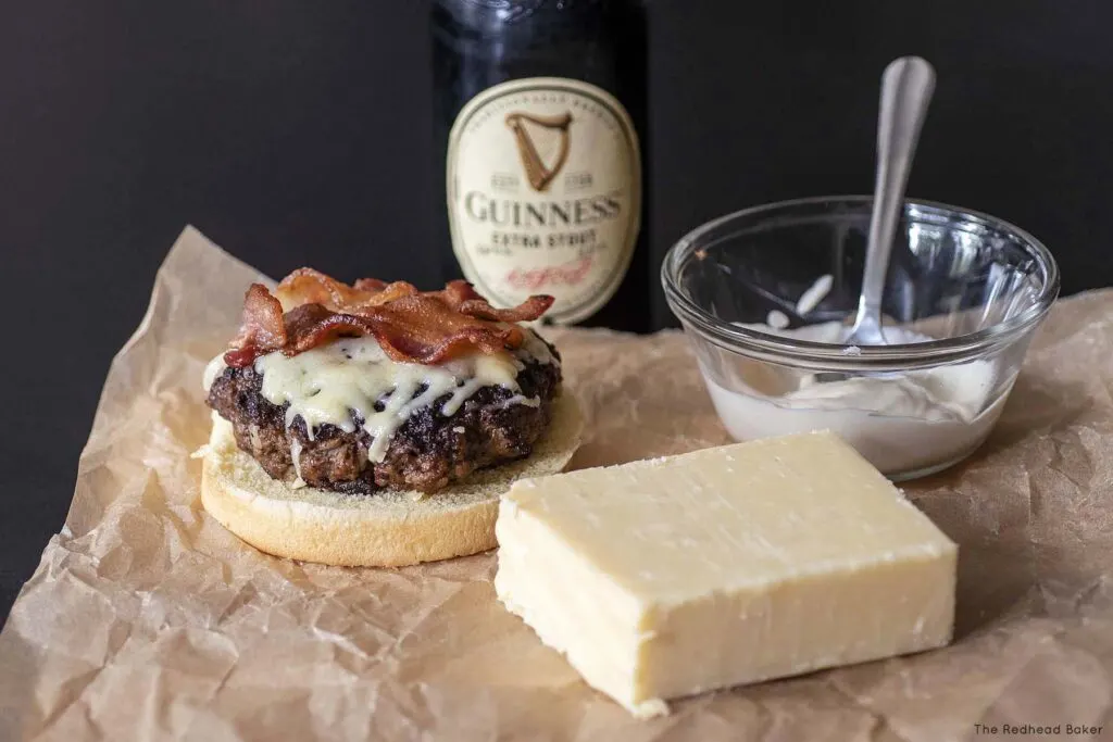 An Irish style burger, a block of Irish cheddar, a bottle of Guinness and a dish of Irish whiskey aioli on a piece of parchment