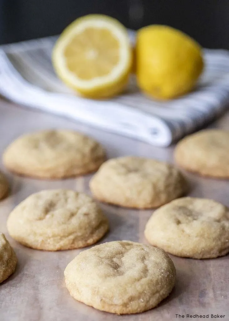 Six lemon doodles on a wooden cutting board in front of two lemon halves on a blue-and-white striped kitchen towel