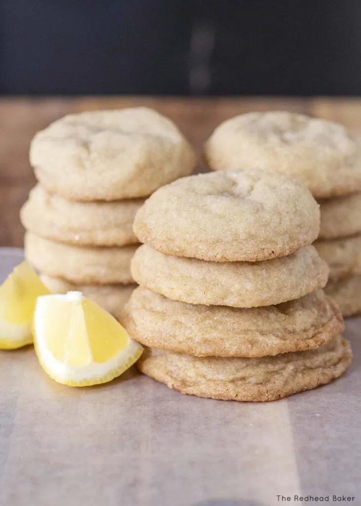 Three stacks of lemon doodles on a wooden cutting board with 2 lemon wedges
