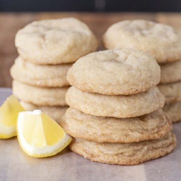 Three stacks of lemon doodles on a wooden cutting board with 2 lemon wedges