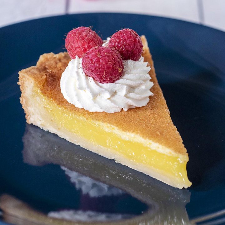 A slice of shortbread lemon tart garnished with whipped cream and raspberries
