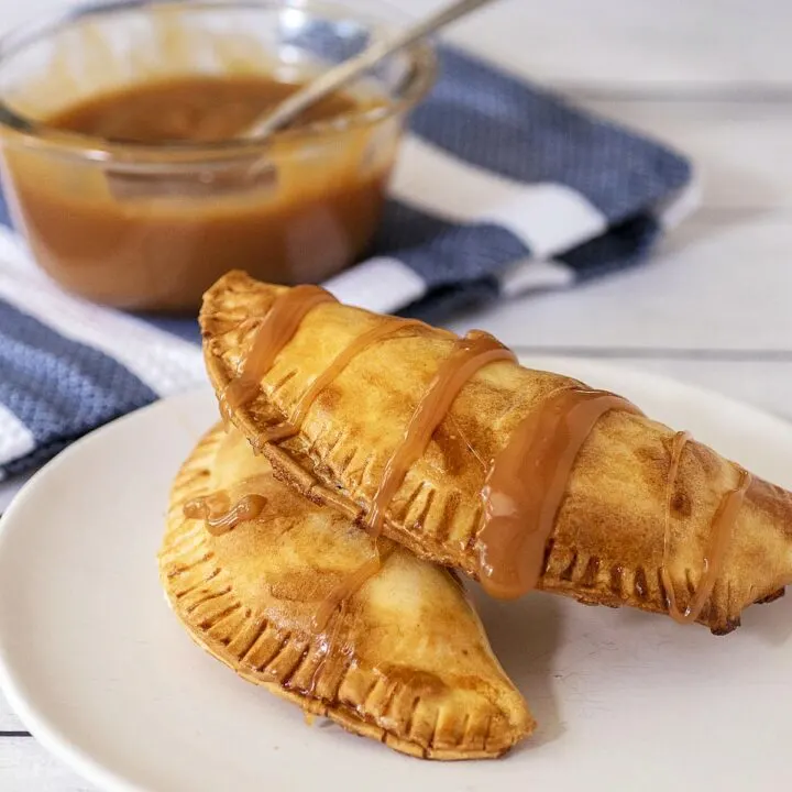 Two air fried empanadas on a plate in front of a dish of caramel sauce.