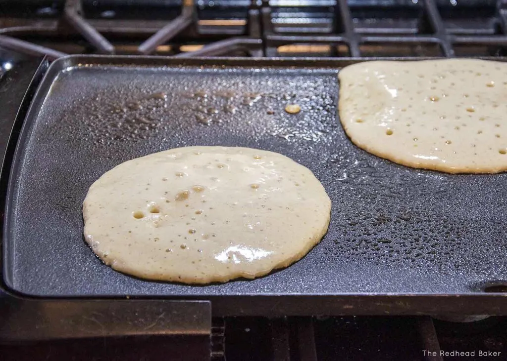 Two oat flour pancakes being cooked on a griddle