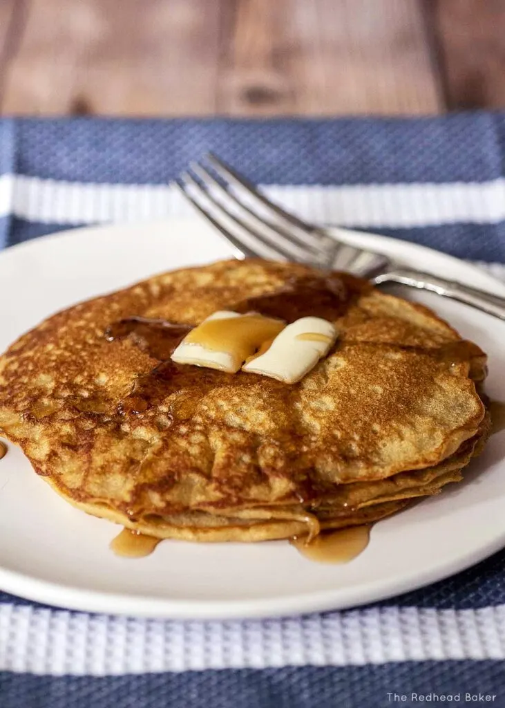 A stack of oat flour pancakes on a white plate with butter and maple syrup