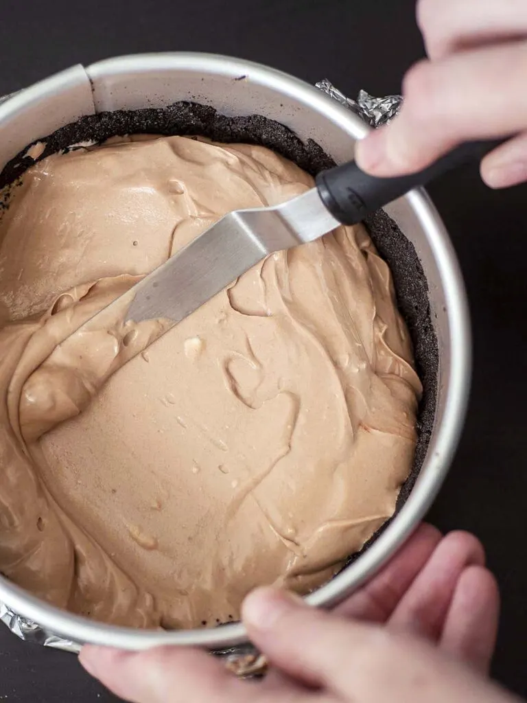 Cheesecake batter being spread into a springform pan.