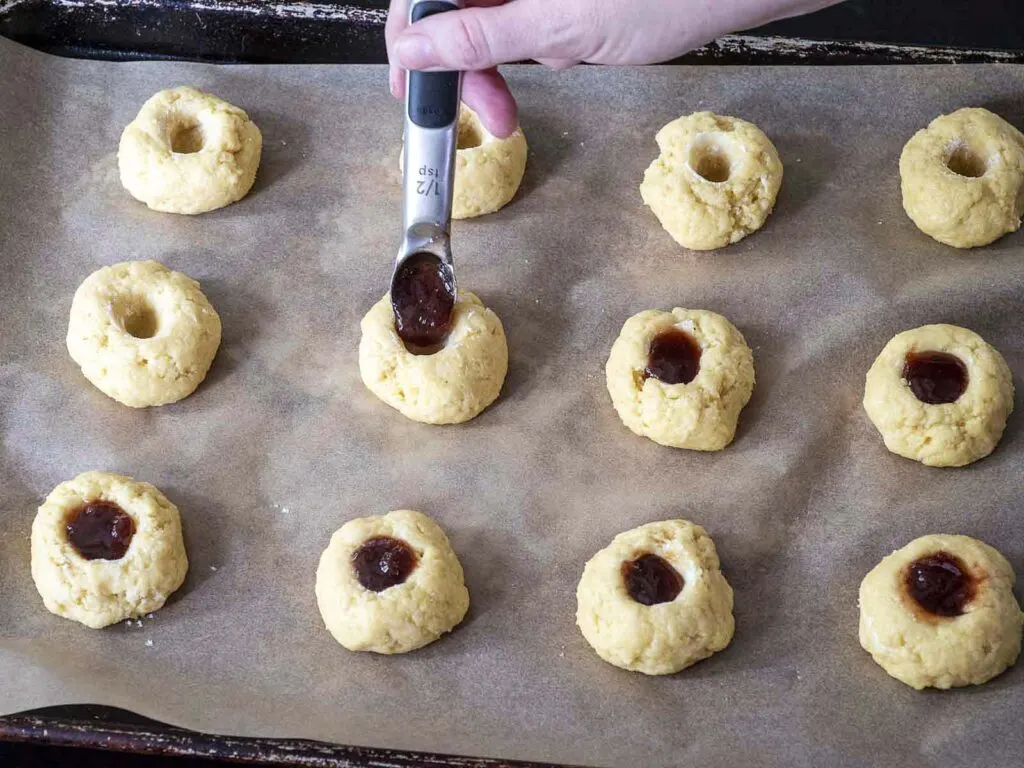 Raspberry jam being spooned into the holes of each dough ball.