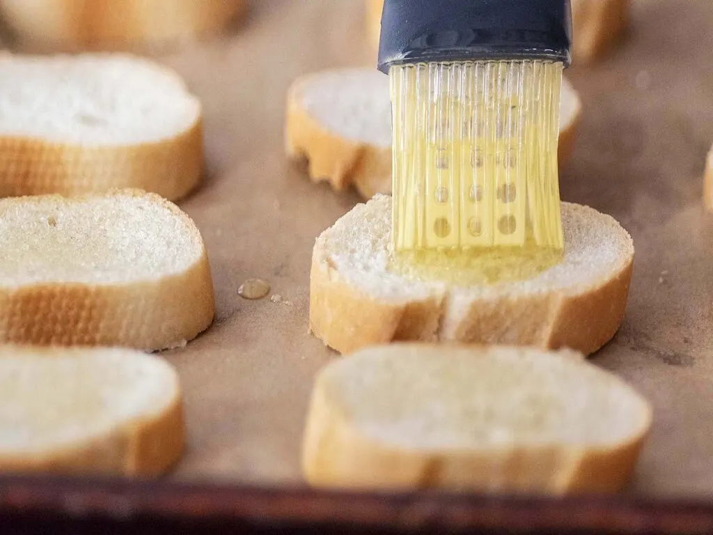 Olive oil being brushed onto baguette slices.
