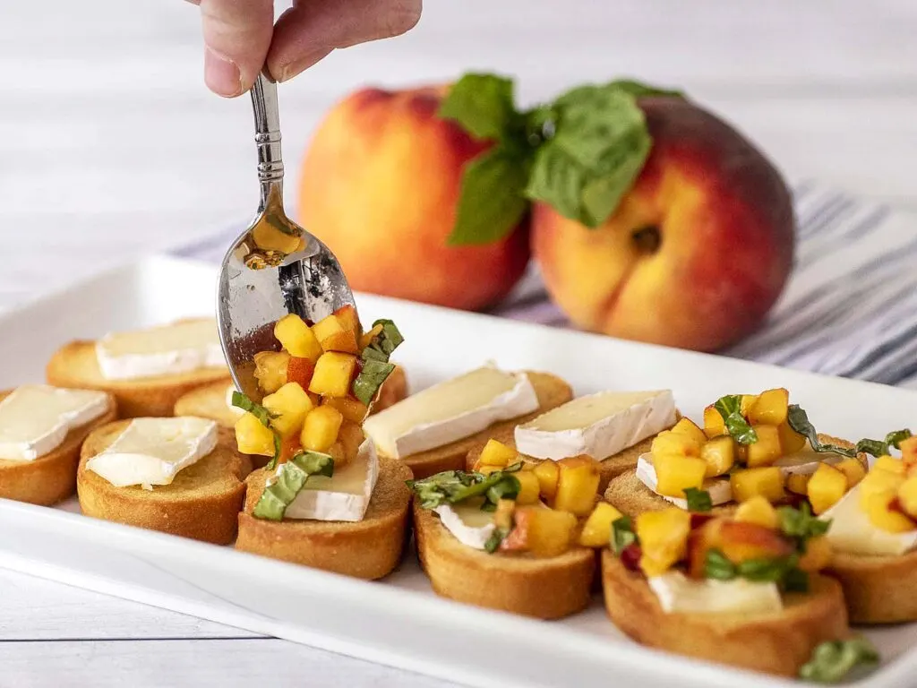 Peach topping being spooned onto toasted baguette slices.