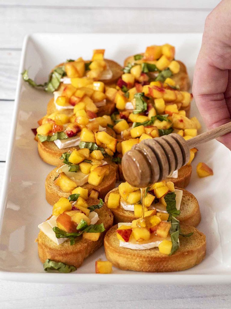 Honey being drizzled onto a tray of peach bruschetta.