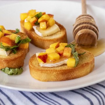 Three pieces of peach bruschetta on a white plate with a honey dipper.