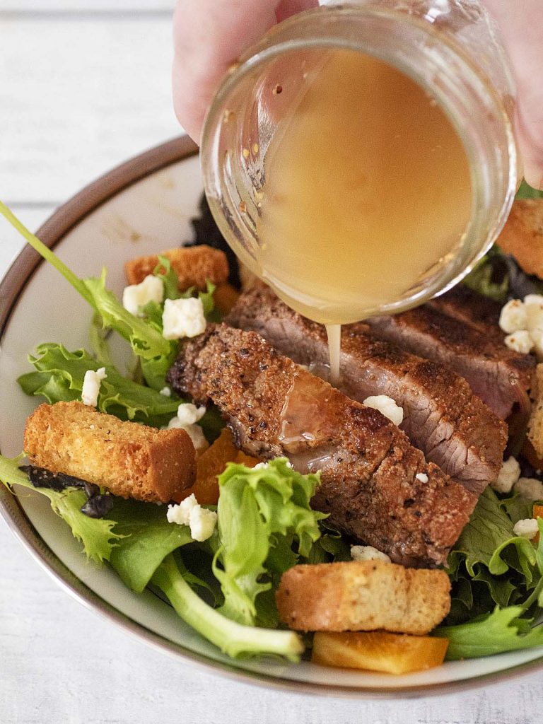 Red wine vinaigrette being poured onto steak and bell pepper salad.