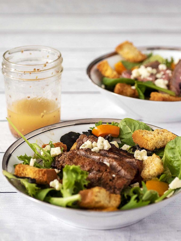 Two bowls of steak and bell pepper salad with a jar of red wine vinaigrette.