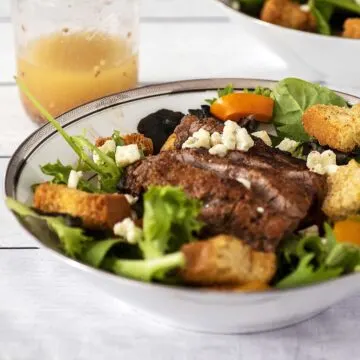 A bowl of steak and bell pepper salad in front of a jar of red wine vinaigrette.