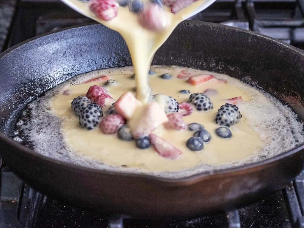 Dutch baby batter being poured into a cast-iron skillet.