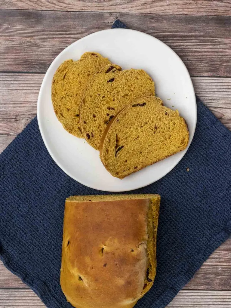 An overhead view of three slices of pumpkin cranberry yeast bread on a white plate.
