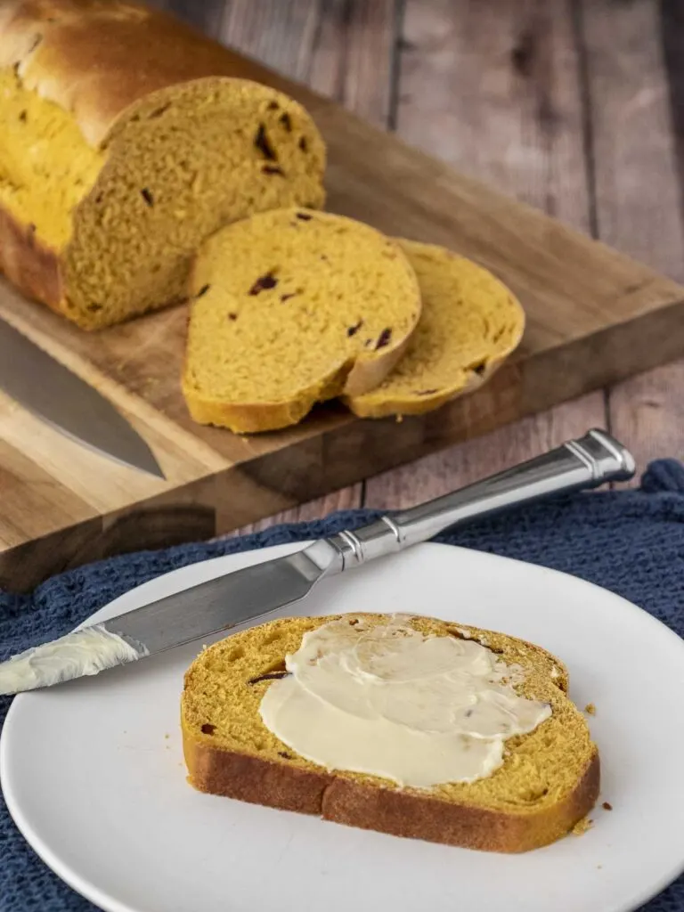 A slice of pumpkin cranberry yeast bread with butter spread on it.