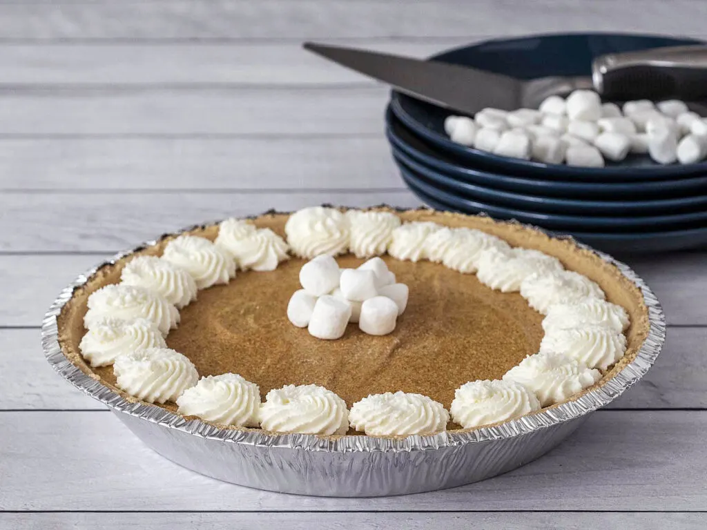 A pumpkin marshmallow pie in front of a stack of dessert plates.